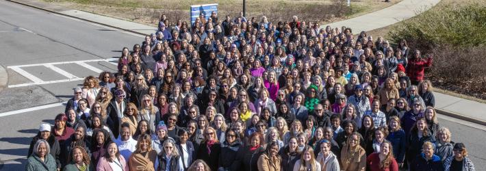 A large group of women gathered for a photo on the street in front of the Katherine G. Johnson Computational Research Facility building.
