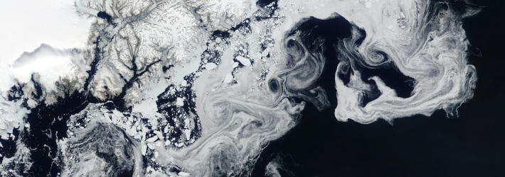 A satellite view of sea ice. The ice is white and solid at top left, while the edges swirl and swoop through the dark blue water.
