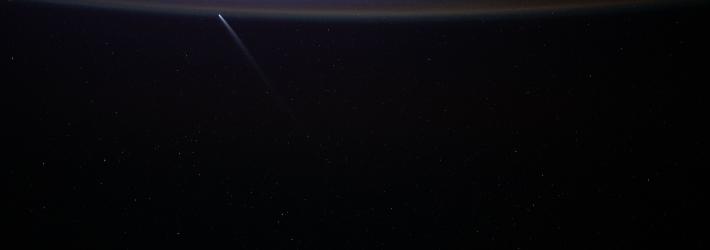 A bright blue arc appears in the darkness of space. The comet streaks upward, almost perpendicular.