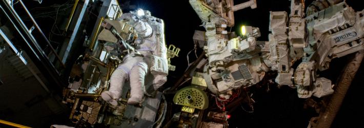 Astronaut Suni Williams (just left of center) wears a white spacesuit while she conducts a spacewalk outside of the International Space Station.