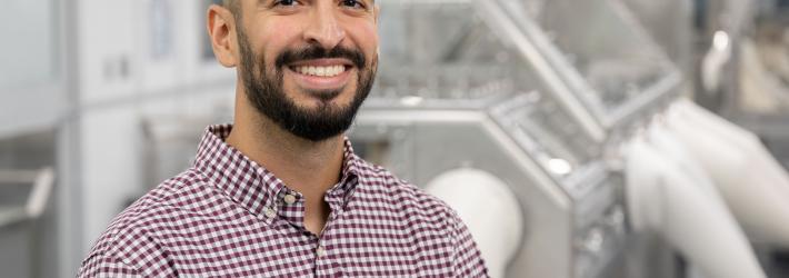 Lead Astromaterial Curation Engineer Salvador Martinez III smiles at the camera wearing a plaid shirt inside the OSIRIS REx Lab.