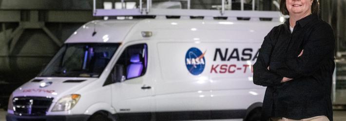 Transportation Officer Melissa Coleman stands in front of a white van with the NASA emblem on it.